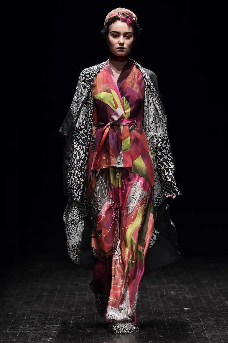A kimono jacket and trousers in red, purple and lime green beneath a black-and-white patterned coat, on the catwalk at Stockholm Fashion Week 2017.