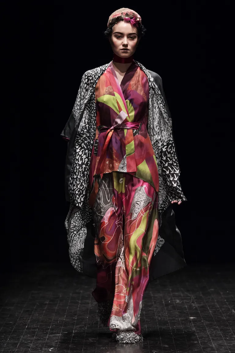 A kimono jacket and trousers in red, purple and lime green beneath a black-and-white patterned coat, on the catwalk at Stockholm Fashion Week 2017.