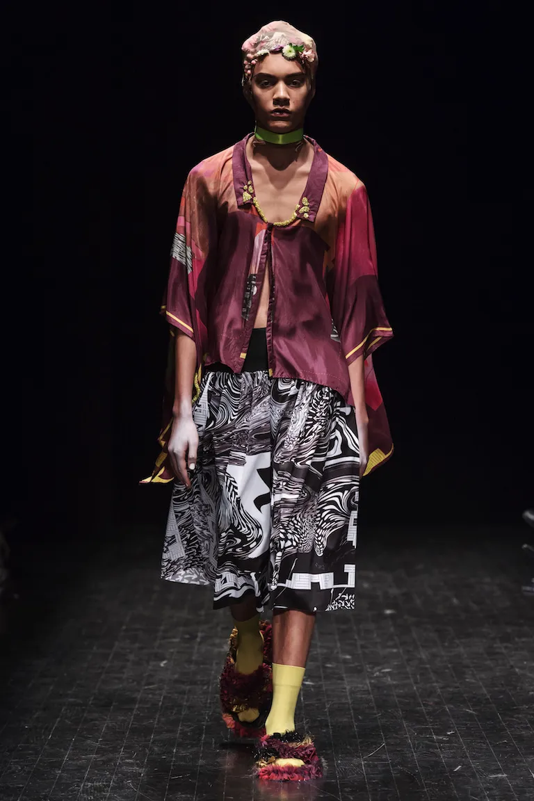 A burgundy silk top over a full skirt in a black-and-white marbled pattern, styled with yellow socks and fringed sandals.