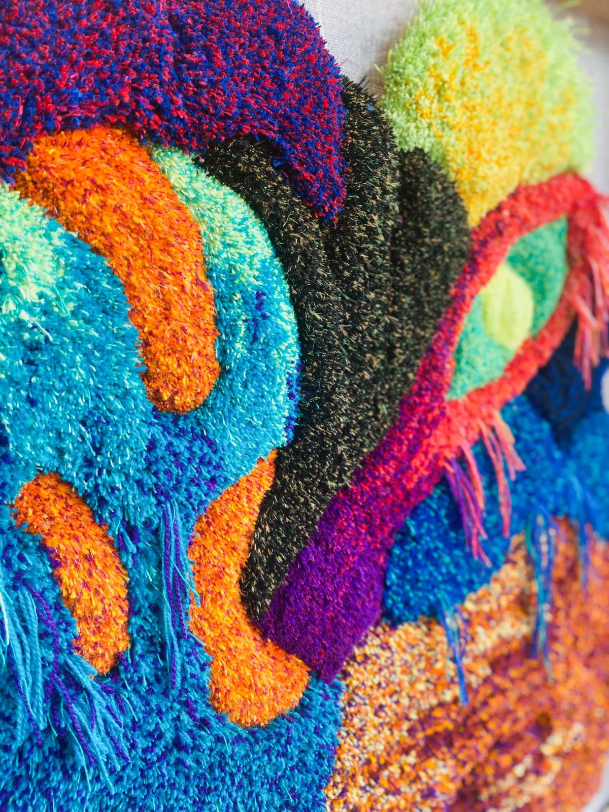 The Monster Garden 1 — detalj av tuftat textilverk i blått, orange och turkos med hängande fransar, av Amandah L'Narte