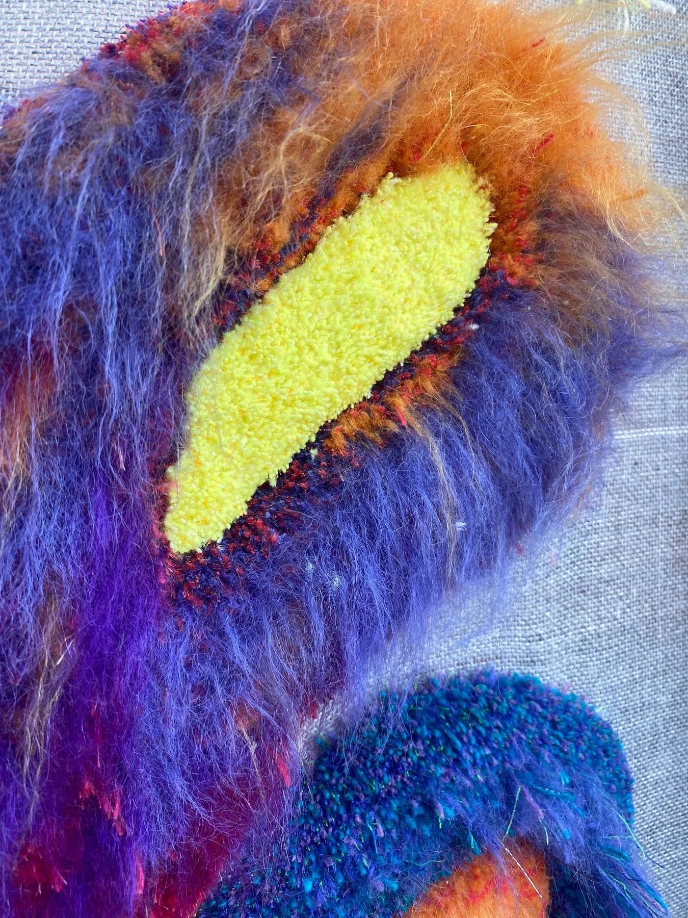 The Monster Garden 2 — detalj: gult tättuftat ögonfält omgivet av långluggig lila och orange mohair, av Amandah L'Narte