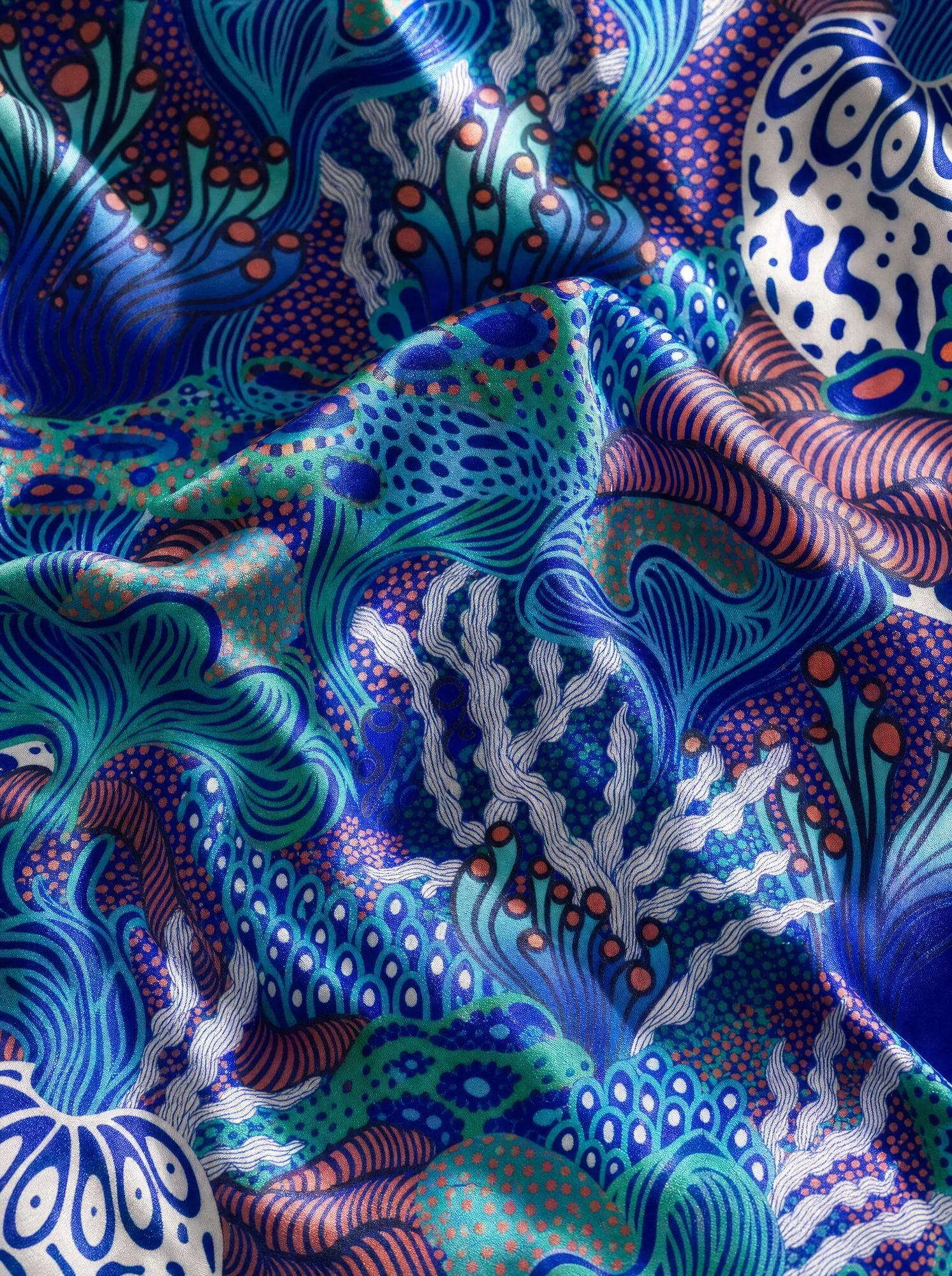 A mock-up presents Coral Garden draped on silk, with coral- and seaweed-like forms in flowing bands, dotted fields and rings in cobalt blue, turquoise and coral.