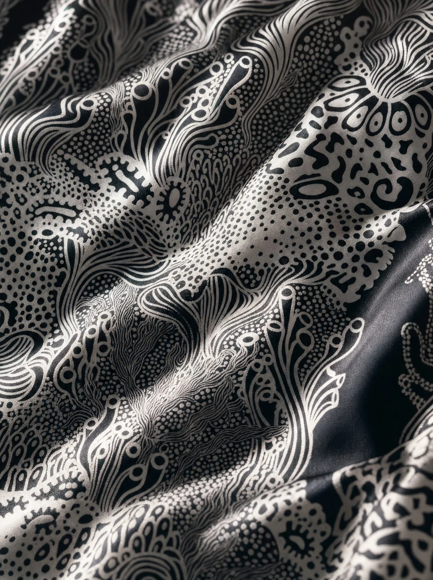 A mock-up presents Coral Garden in a monochrome colourway, black against off-white across folded silk, bringing out the coral forms’ lines and dotted textures.