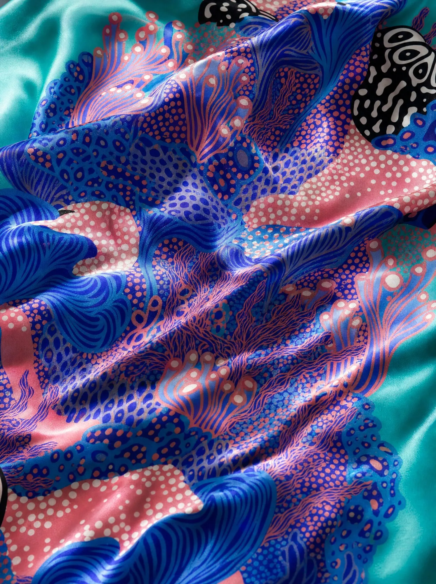 A mock-up presents Coral Garden in cobalt blue and coral pink against turquoise, with dotted and striped coral forms across draped silk.