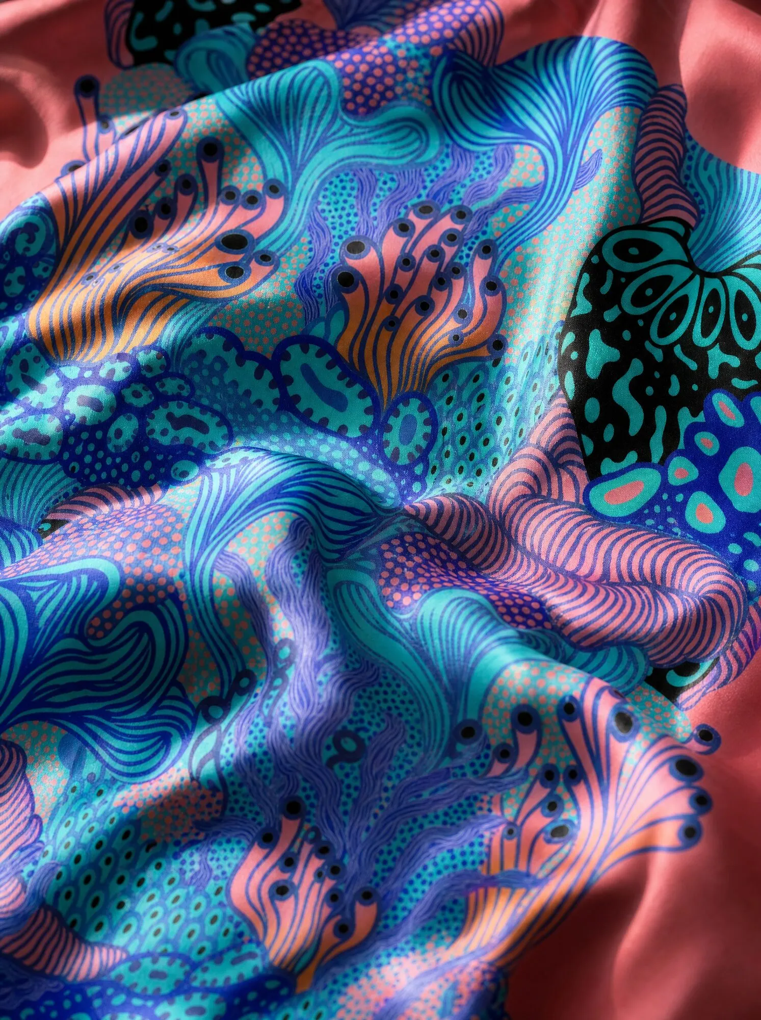 A visualisation presents Coral Garden on draped fabric, with turquoise and aquamarine coral forms, black dots and eye-like rings against coral pink.