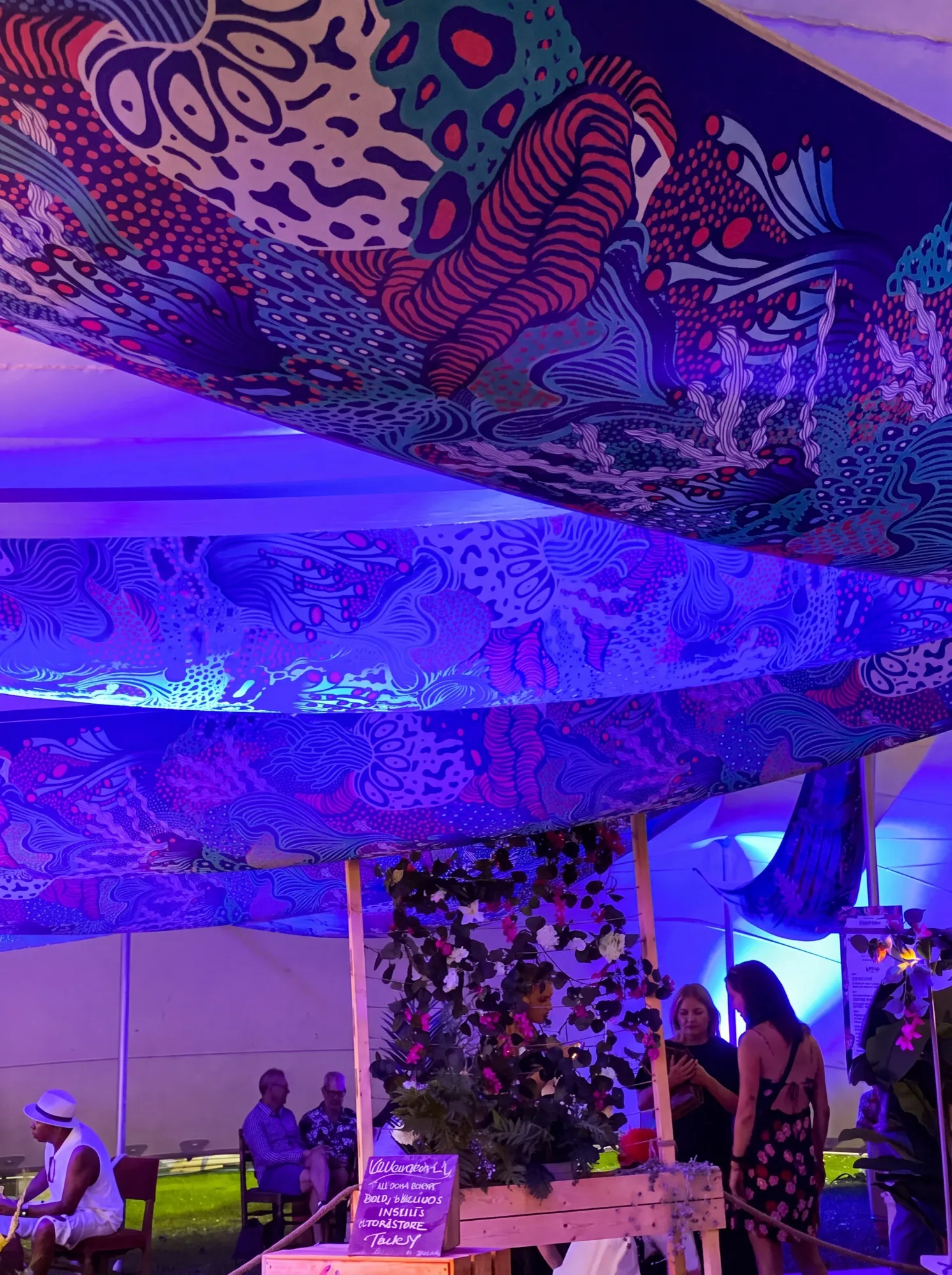 Viewed from below, layered lengths of Coral Garden form a canopy above the bar, with coral forms and dotted fields in blue, pink and off-white under violet evening light.
